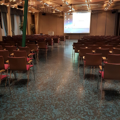 Kleiner Saal in Reihenbestuhlung mit Blick zur Leinwand, beleuchtet